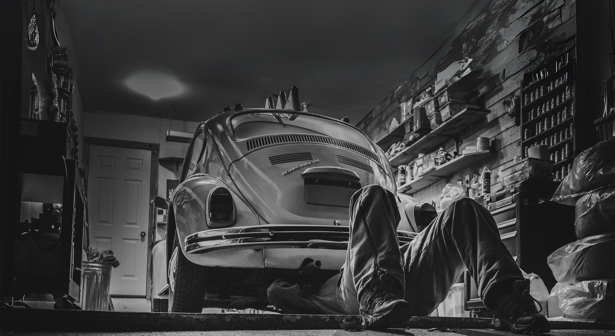 Ein alter VW Käfer in einer Werkstatt wo ein Mechaniker am Unterboden des Auto arbeitet